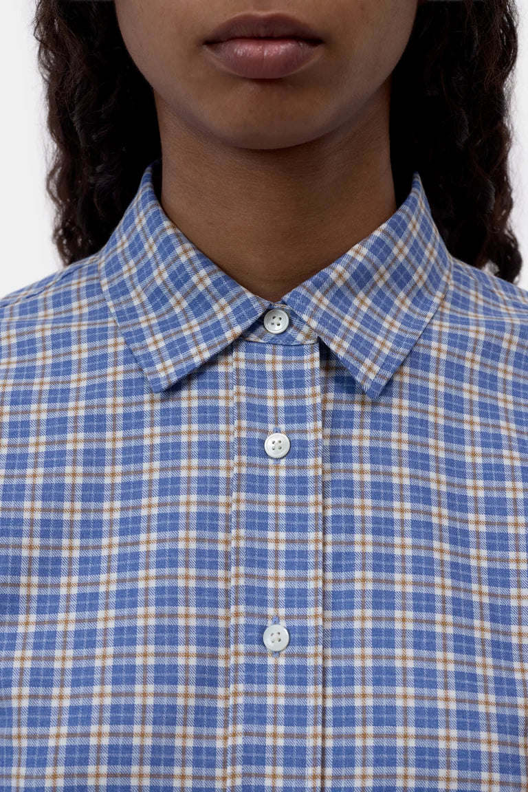 Close-up of a person wearing a blue and beige plaid button-down shirt with a pointed collar and white buttons.
