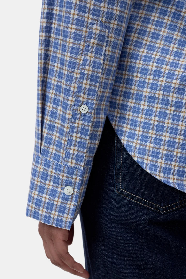 Close-up of a person wearing a blue and beige plaid button-up shirt with dark denim jeans, showing the sleeve, buttons, and side pocket area against a light gray background.