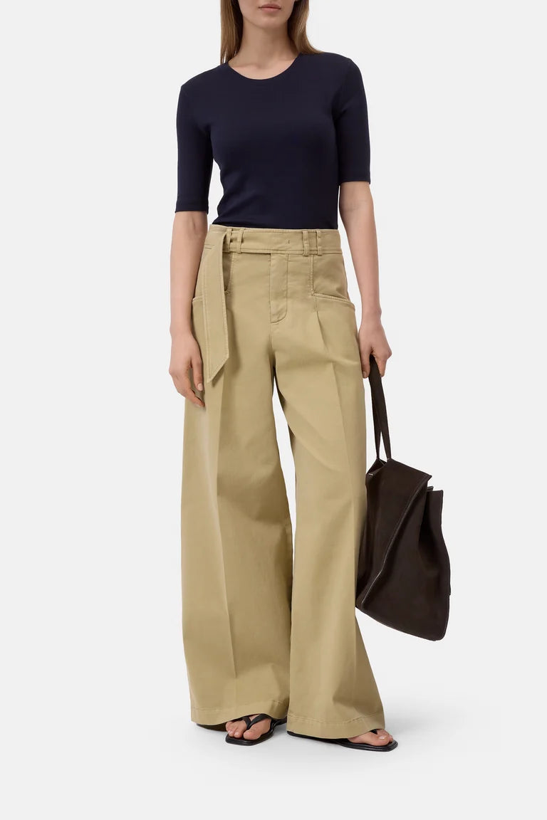 Woman wearing a navy top and beige wide-leg pants, holding a brown bag on a white background