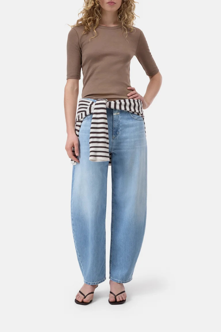 Woman wearing a brown top and light blue jeans with a striped sweater over her shoulder on a white background