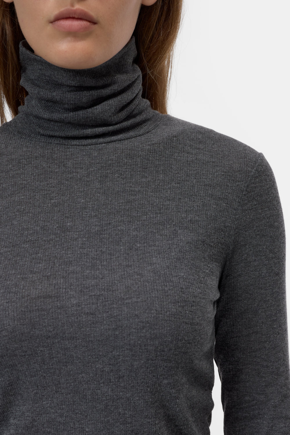 Close-up of a model wearing a dark gray ribbed turtleneck sweater against a plain white background.