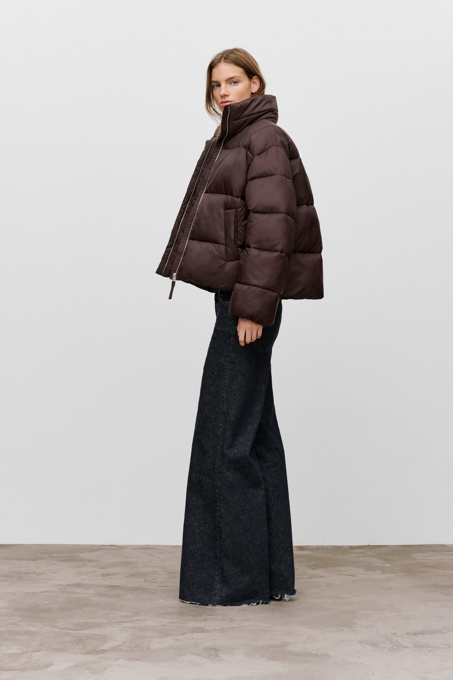 Woman wearing a brown puffer jacket and black pants on a white background