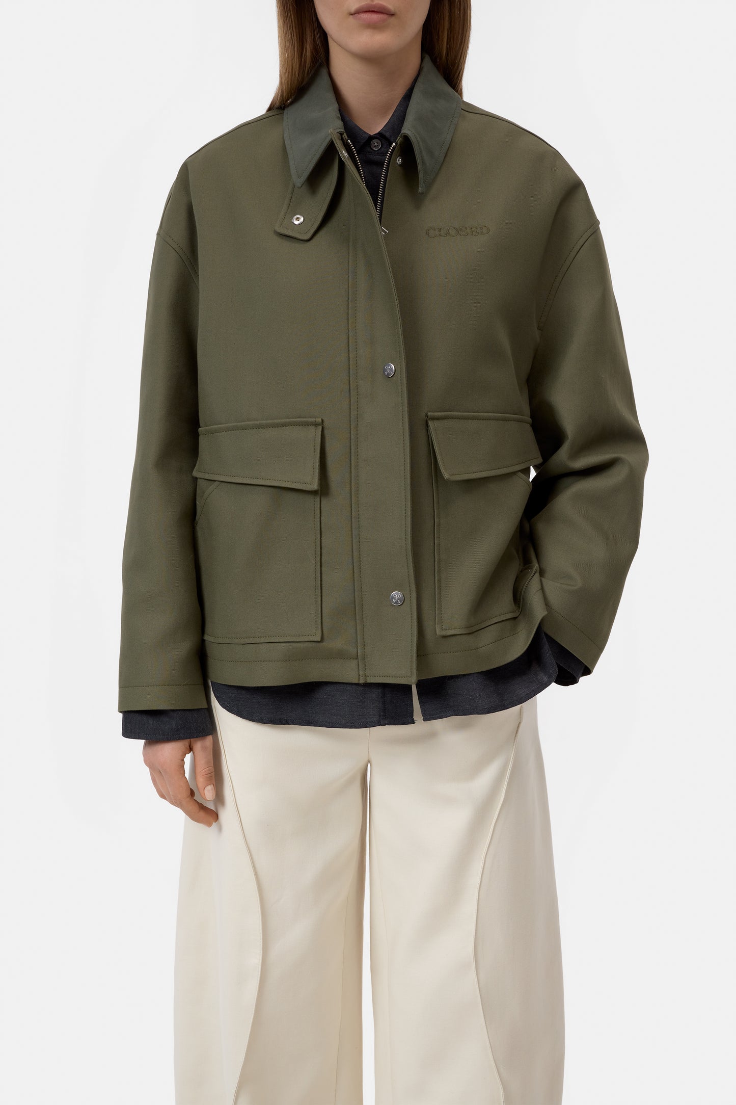 Person wearing a green jacket with two front pockets on a white background