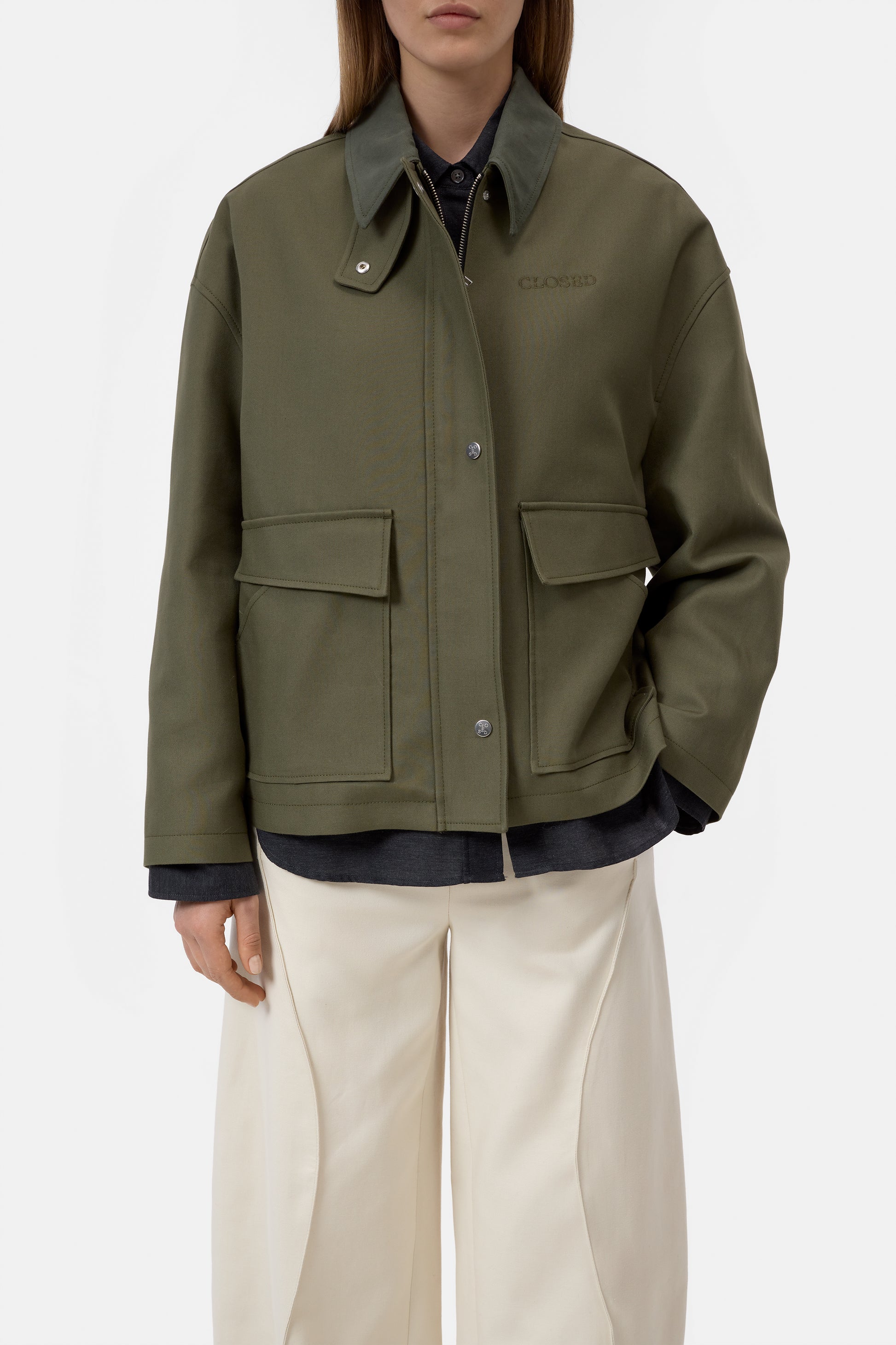 Person wearing a green jacket with two front pockets on a white background