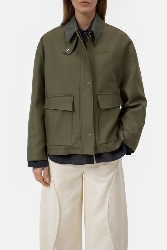 Person wearing a green jacket with two front pockets on a white background