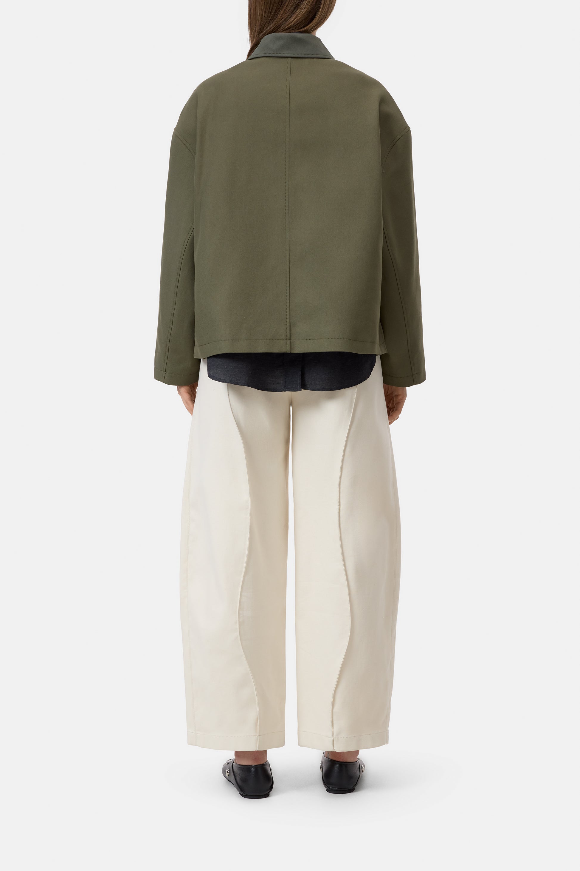 Person wearing a green jacket and white pants on a white background