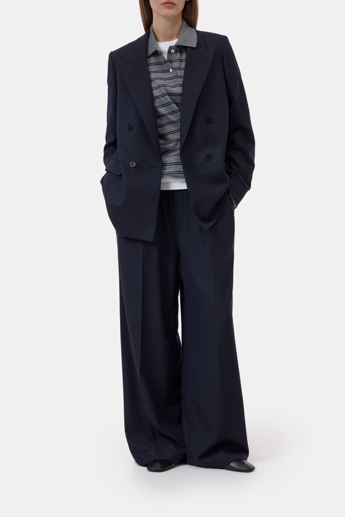 A model wearing a dark navy double-breasted blazer and matching wide-leg trousers, styled with a gray and white striped knit top and a white undershirt, against a plain light gray studio background.