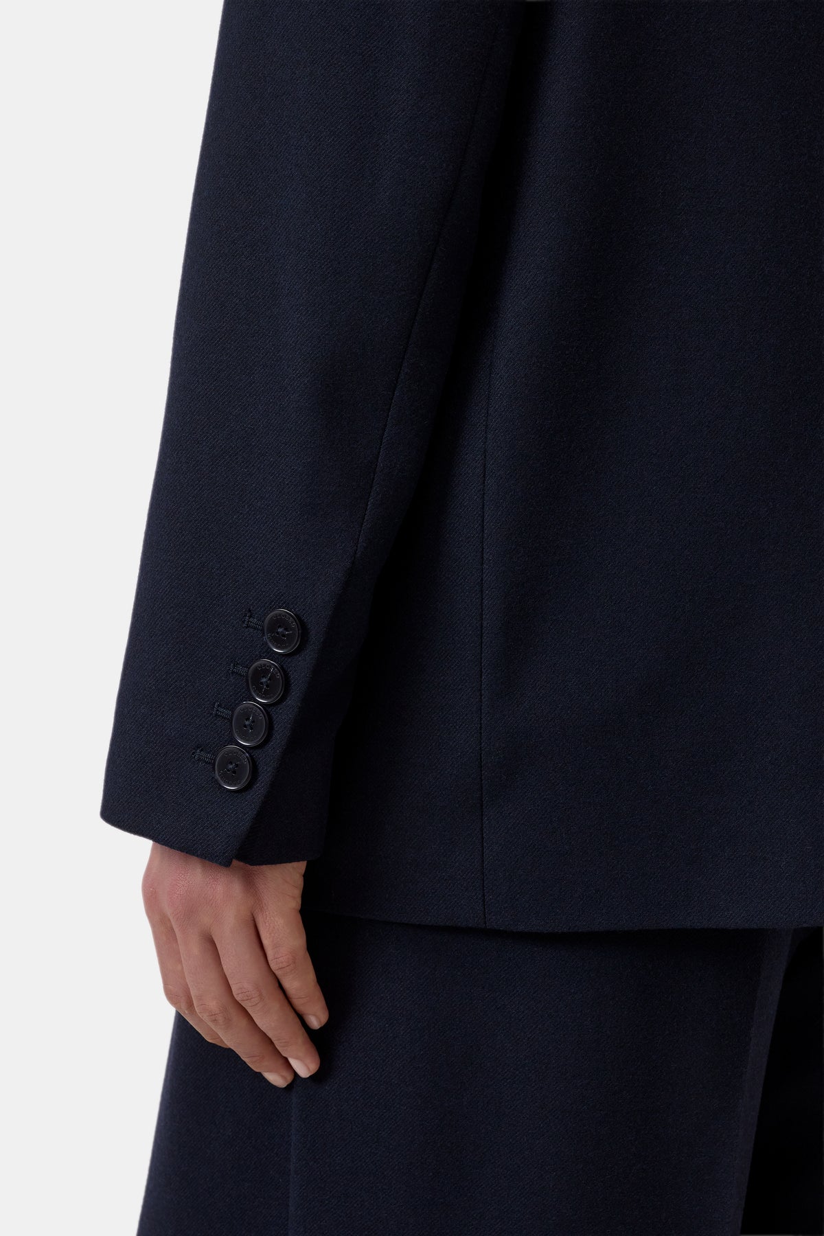 Close-up of a dark navy suit jacket sleeve with four buttons on the cuff, worn with matching navy trousers, against a light gray background.