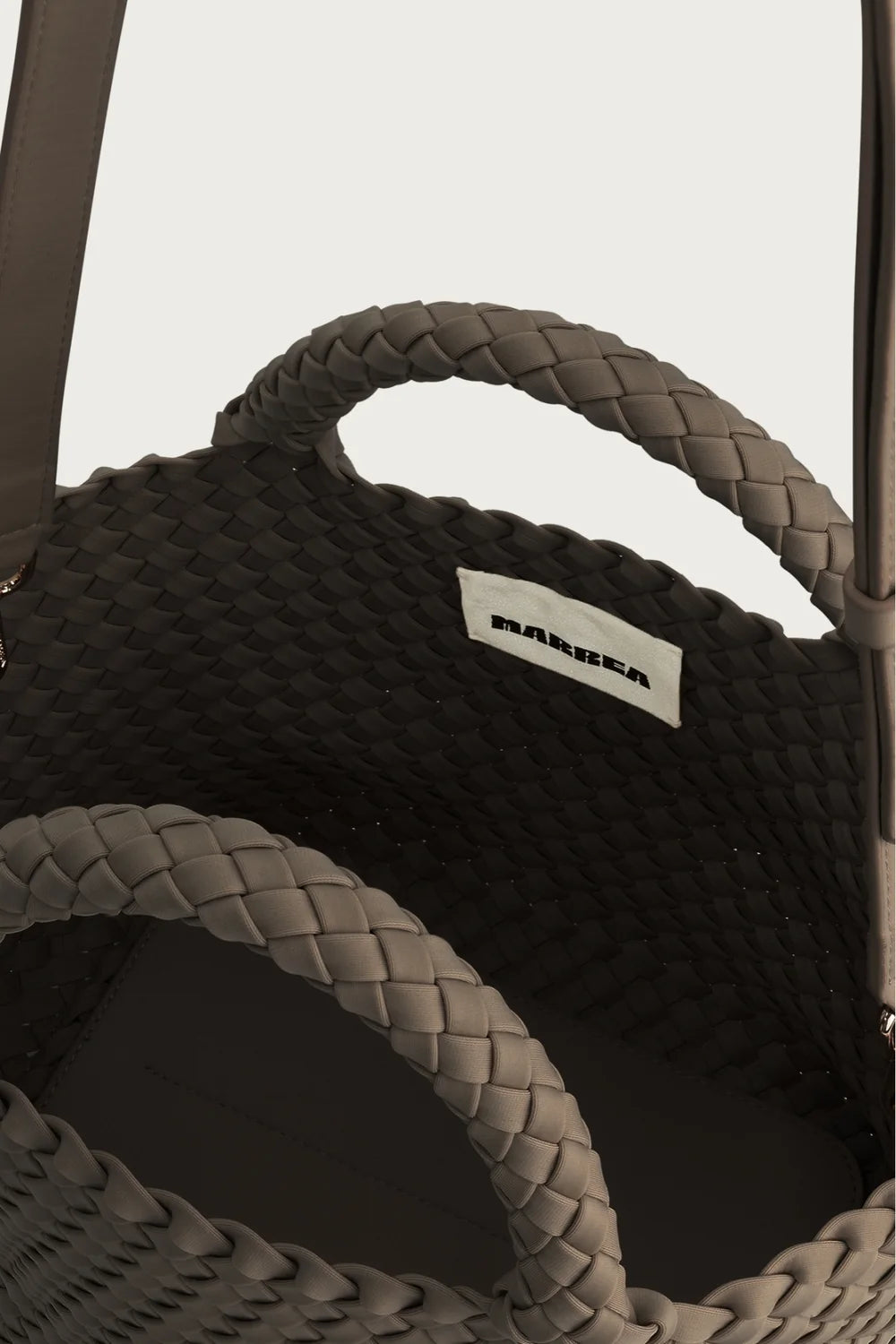 Close-up of a black sandal with braided details and a visible brand label on a light gray background.
