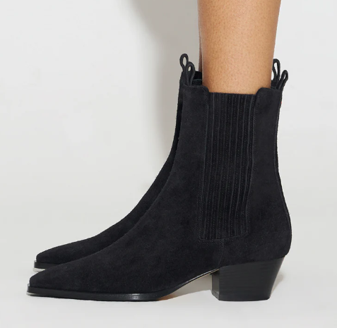 Black suede ankle boots with a ribbed elastic side panel and low block heel, shown on a model's feet against a light gray studio background.