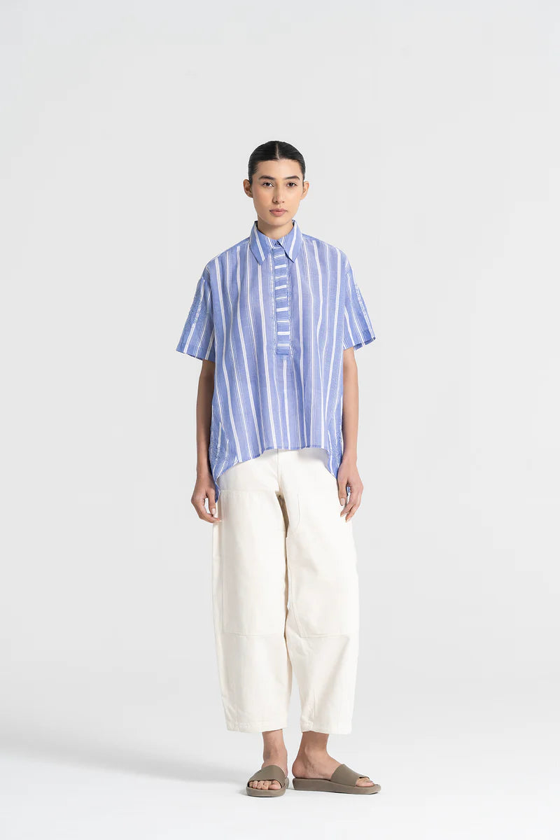 Person wearing a blue striped shirt and white pants on a light gray background
