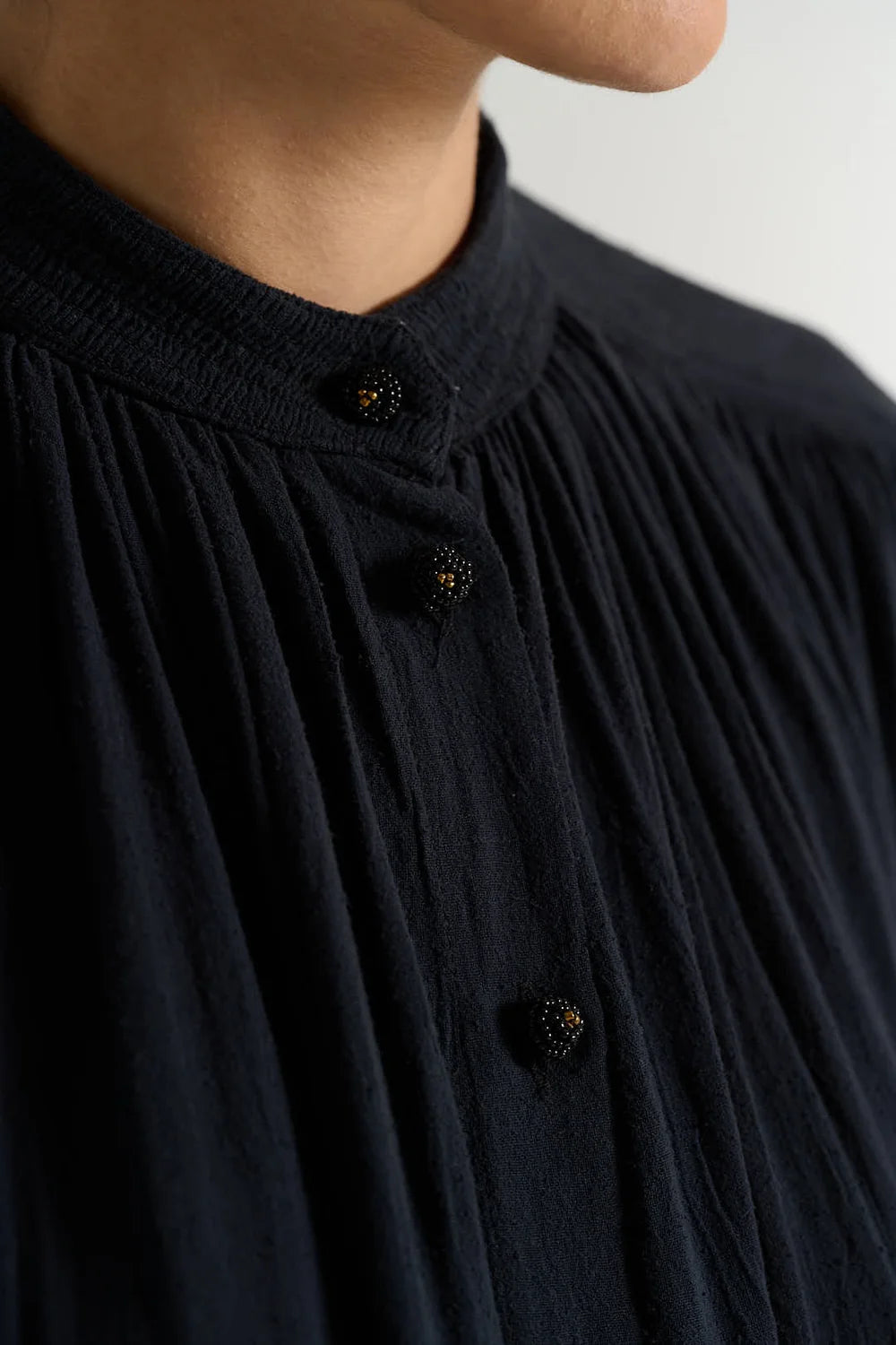 Details of a dark navy long-sleeve blouse with a high gathered collar and front buttons