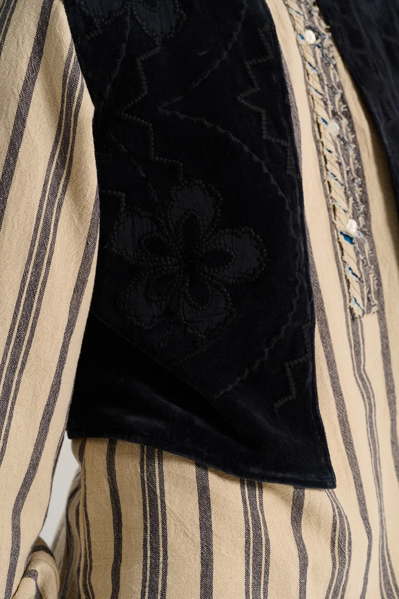Close-up of a traditional garment featuring a black velvet embroidered sleeve with a floral motif and a beige and black vertically striped body.
