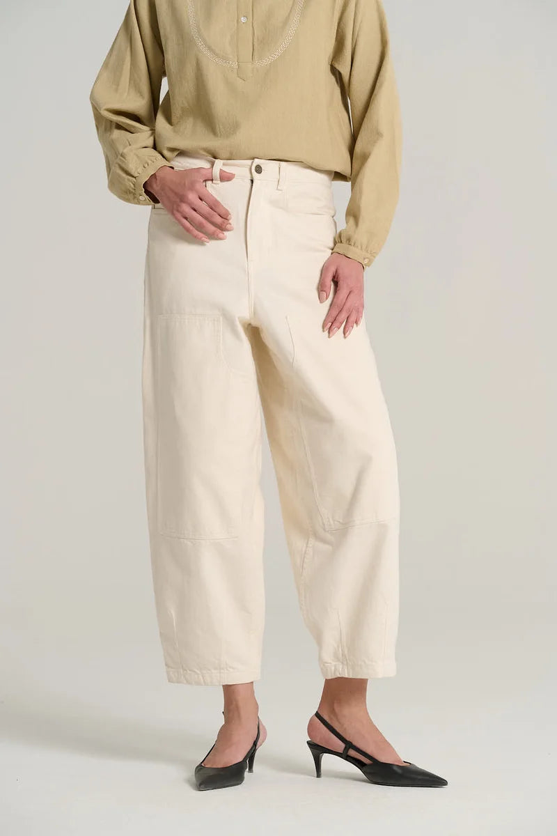 A model wearing off-white cropped wide-leg trousers with a beige long-sleeve blouse and black slingback heels, photographed against a light gray studio background.