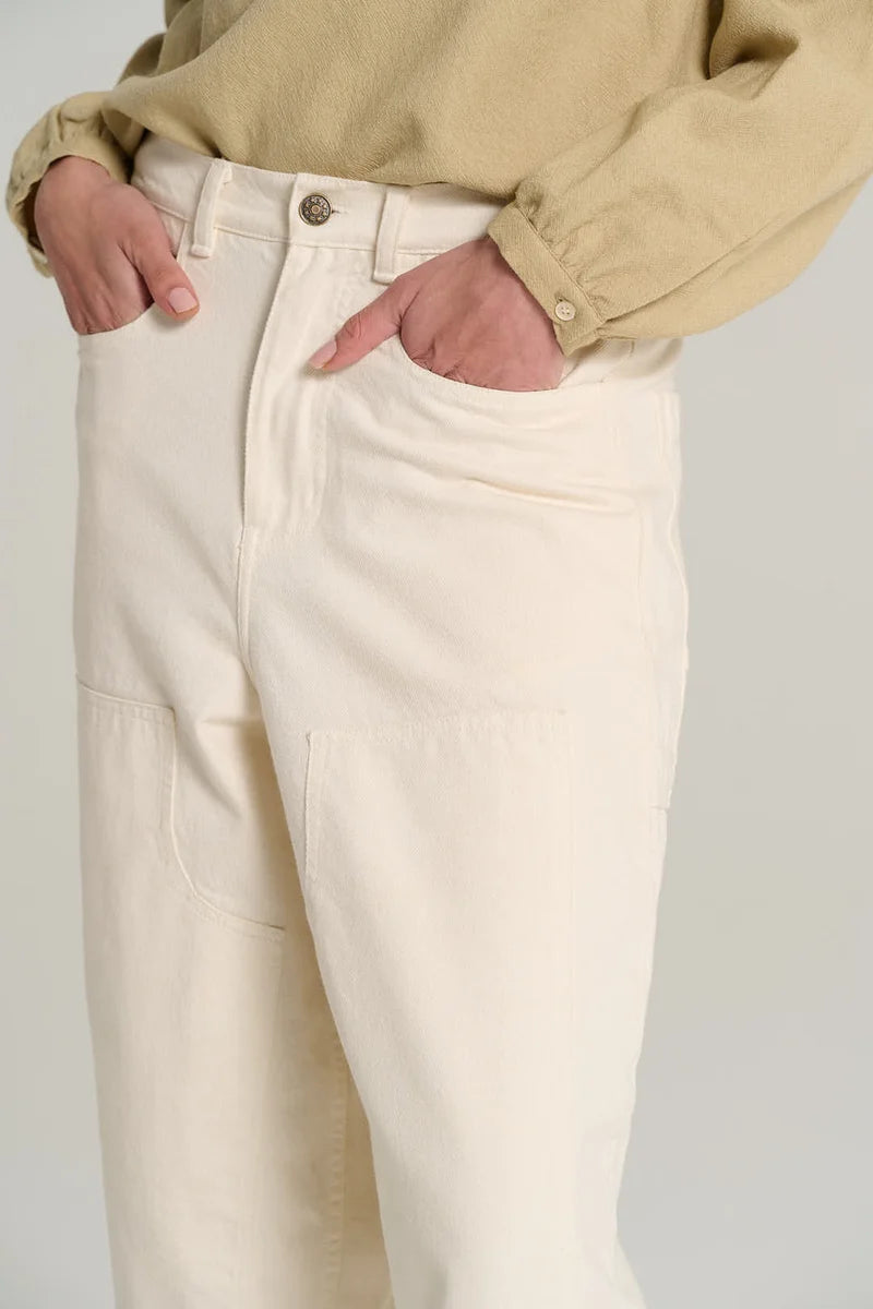 Close-up of a person wearing off-white or cream wide-leg cargo pants with a beige long-sleeve shirt tucked in, standing against a light gray studio background.