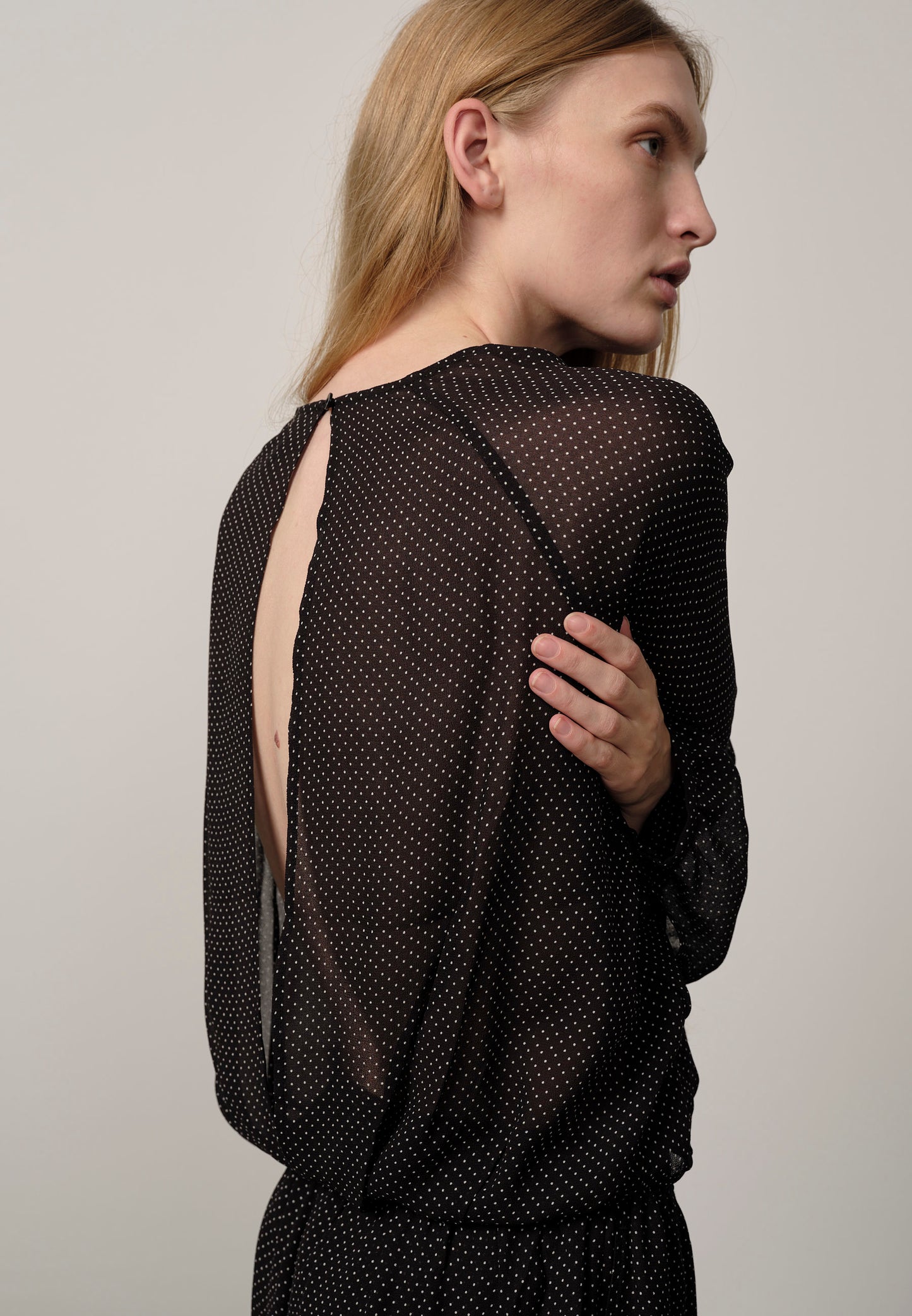 Woman wearing a black mesh top with cut-out design on a plain background