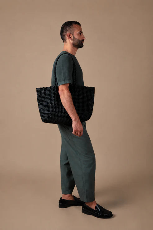 Man holding a black textured bag against a beige background