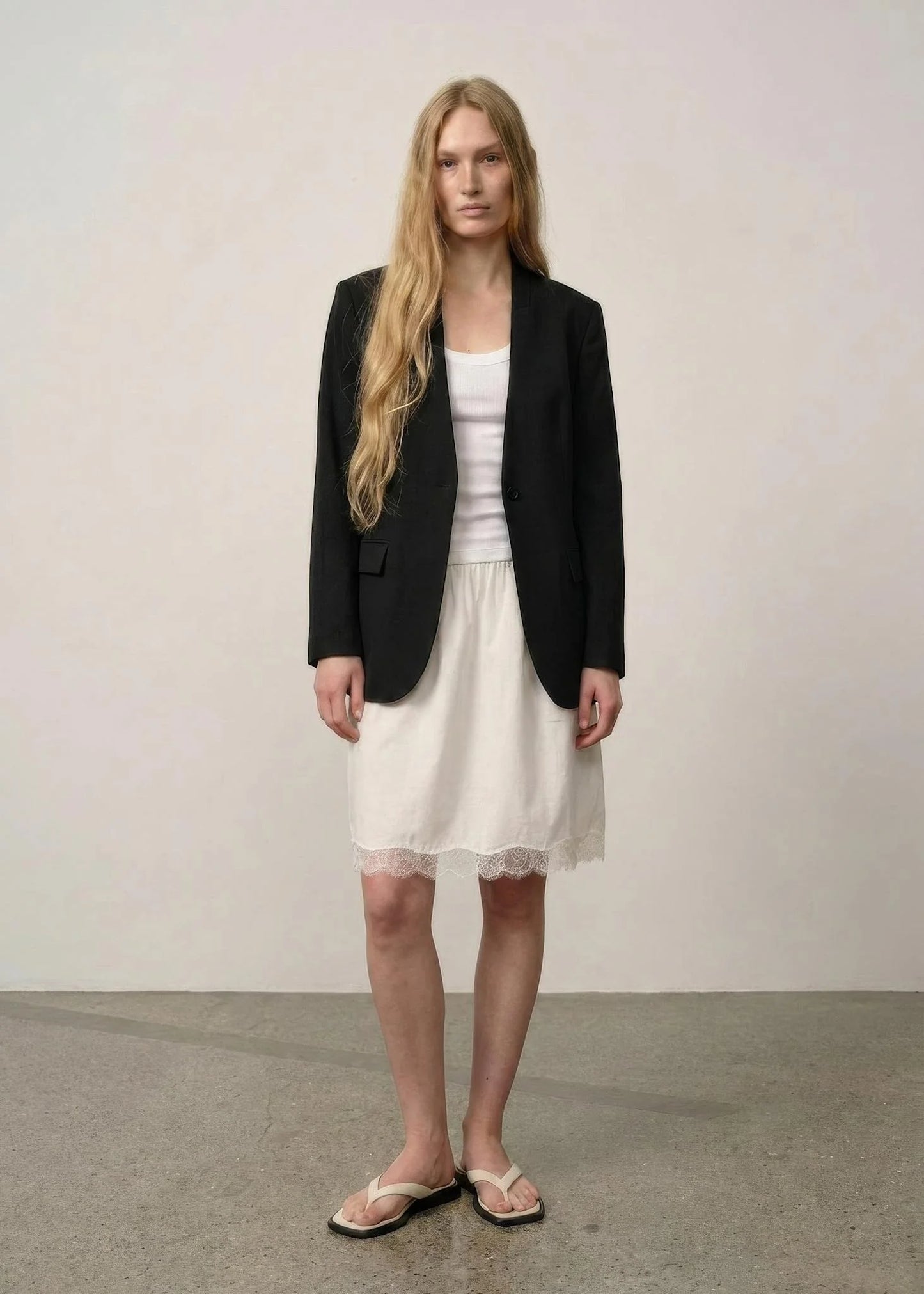 Woman wearing a black blazer over a white top and skirt on a plain background