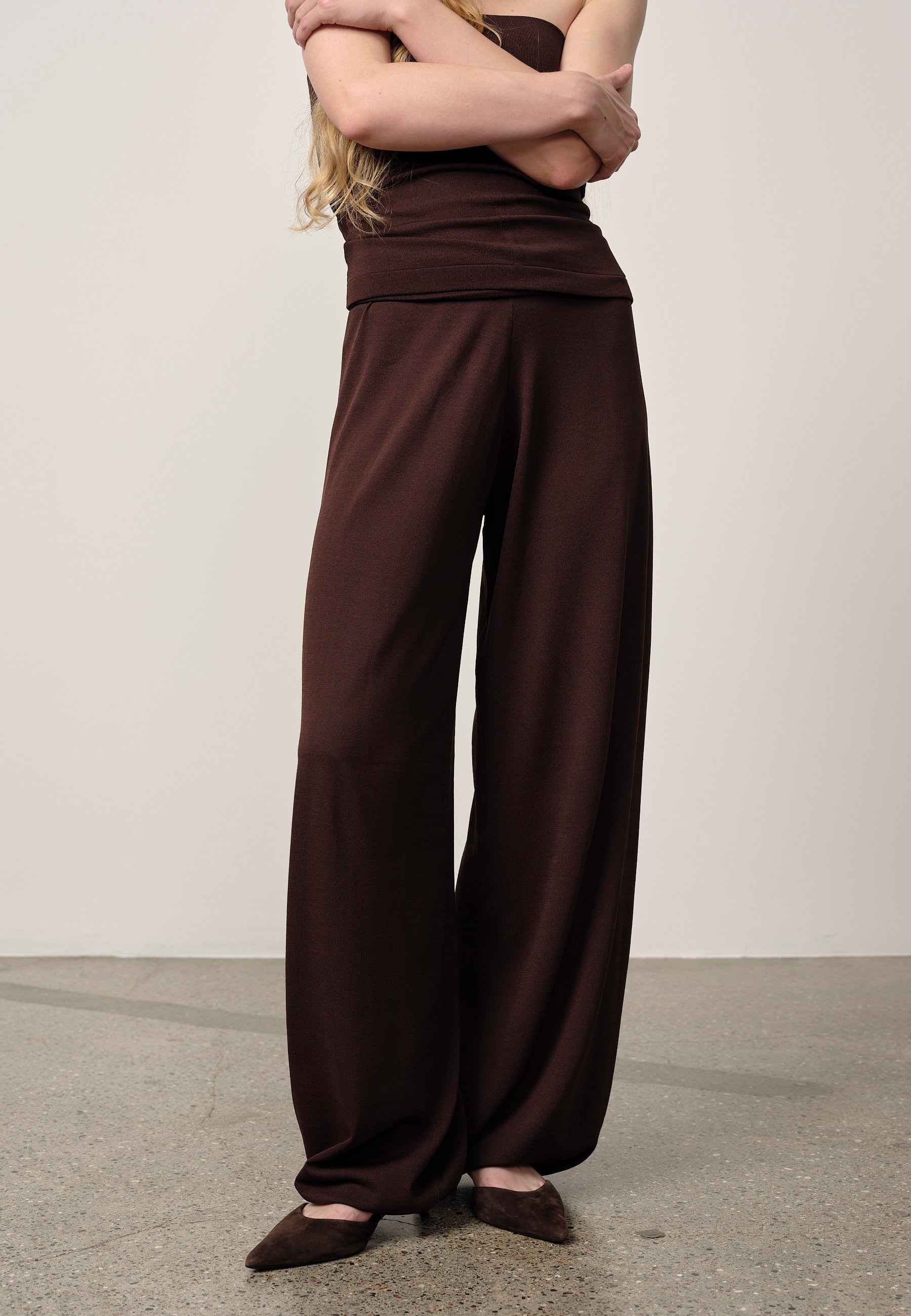 Person wearing brown high-waisted pants and top on a plain background