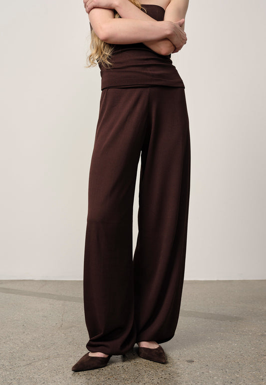 Person wearing brown high-waisted pants and top on a plain background