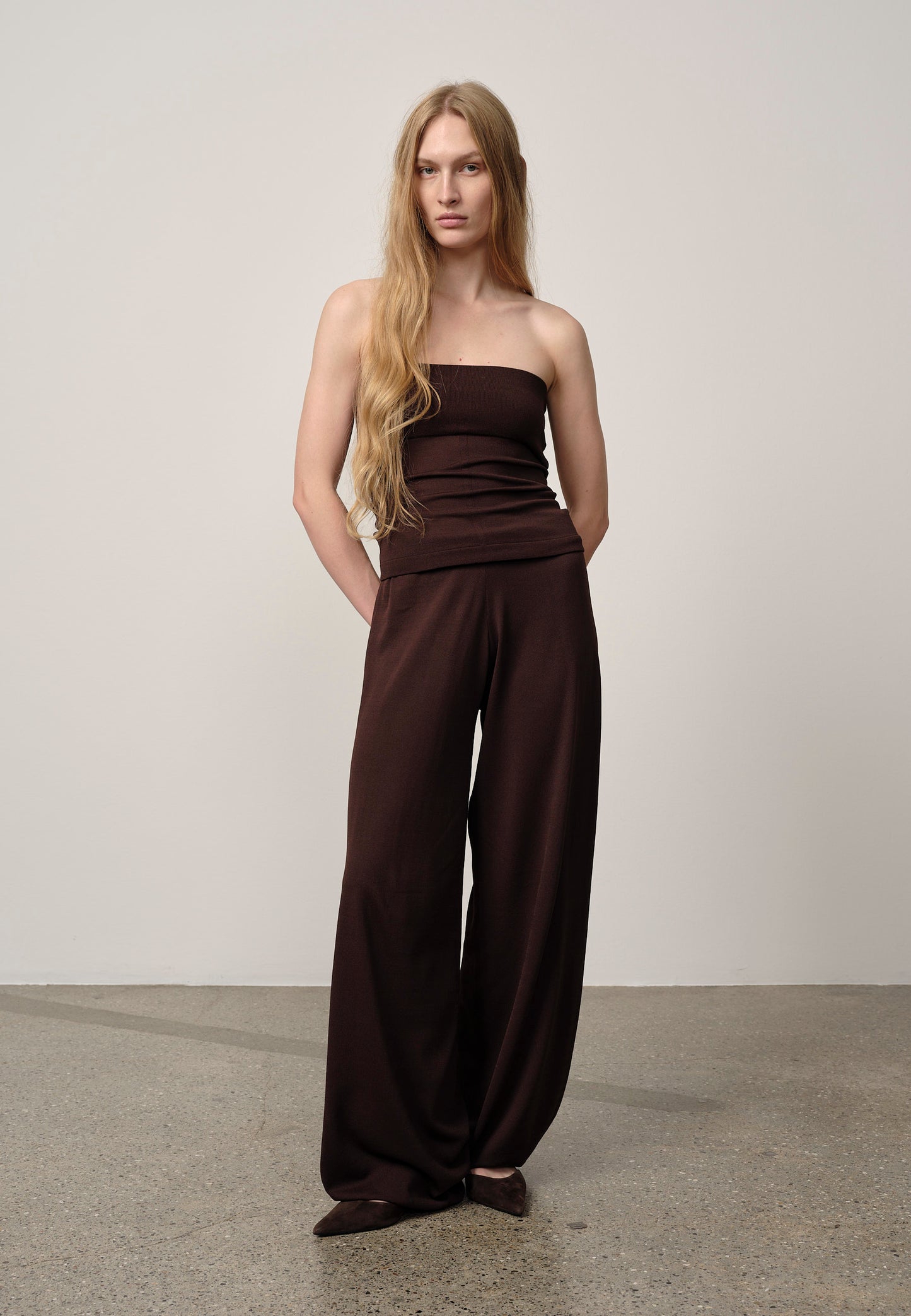 Woman wearing a brown strapless jumpsuit against a plain background