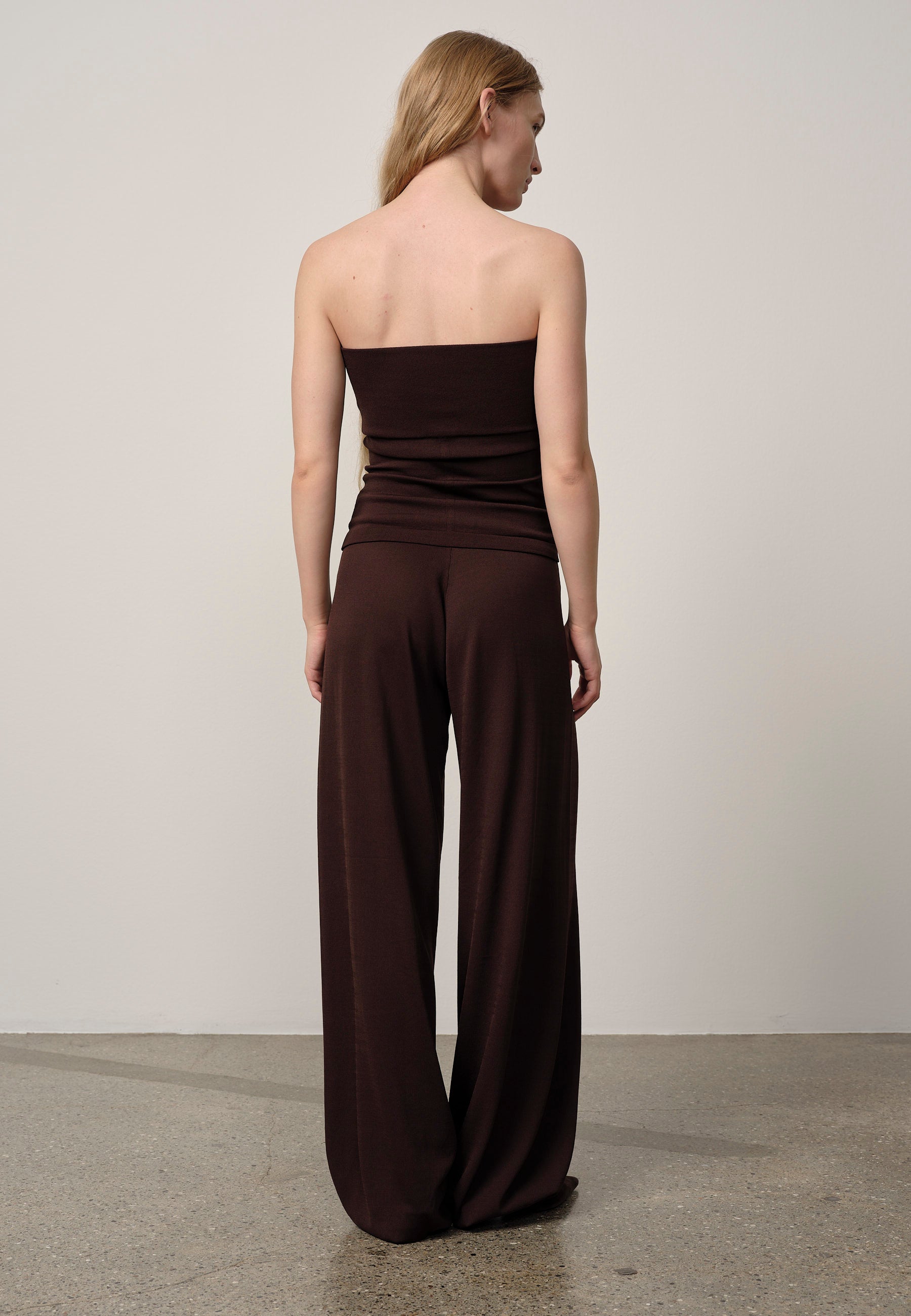 Woman wearing a strapless brown jumpsuit against a plain background