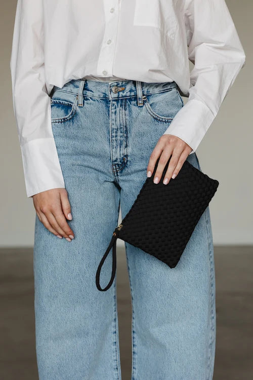 Person wearing a white shirt and blue jeans holding a black clutch.