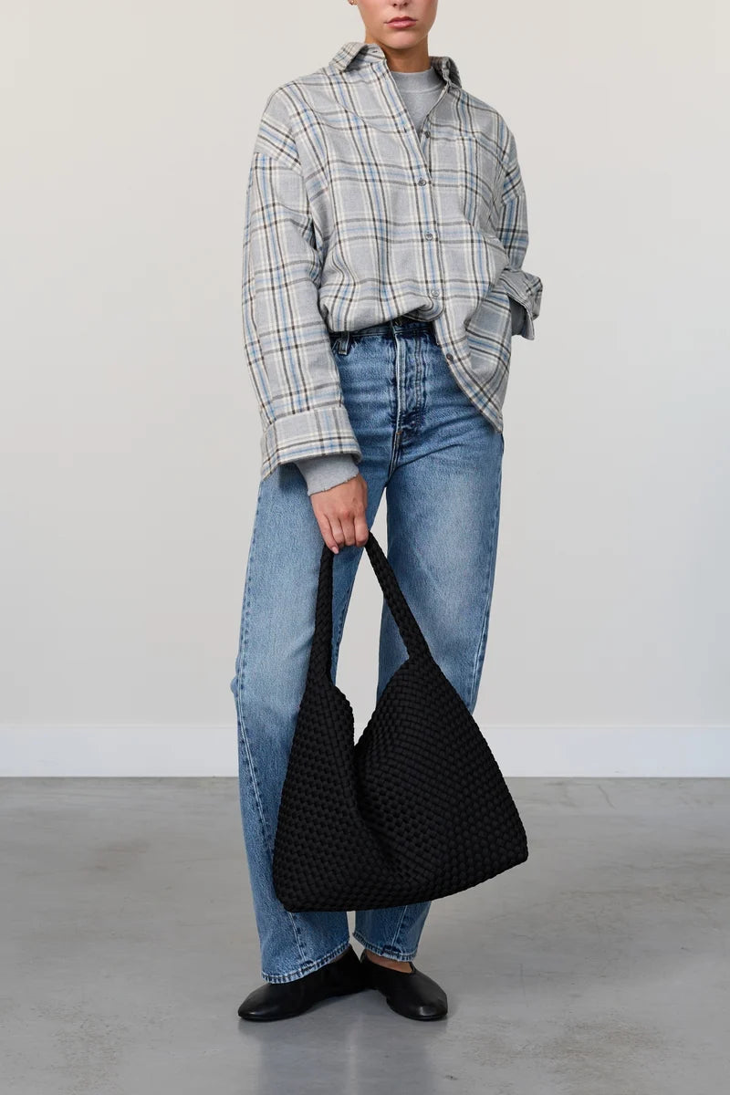 Person holding a black woven handbag against a plain background