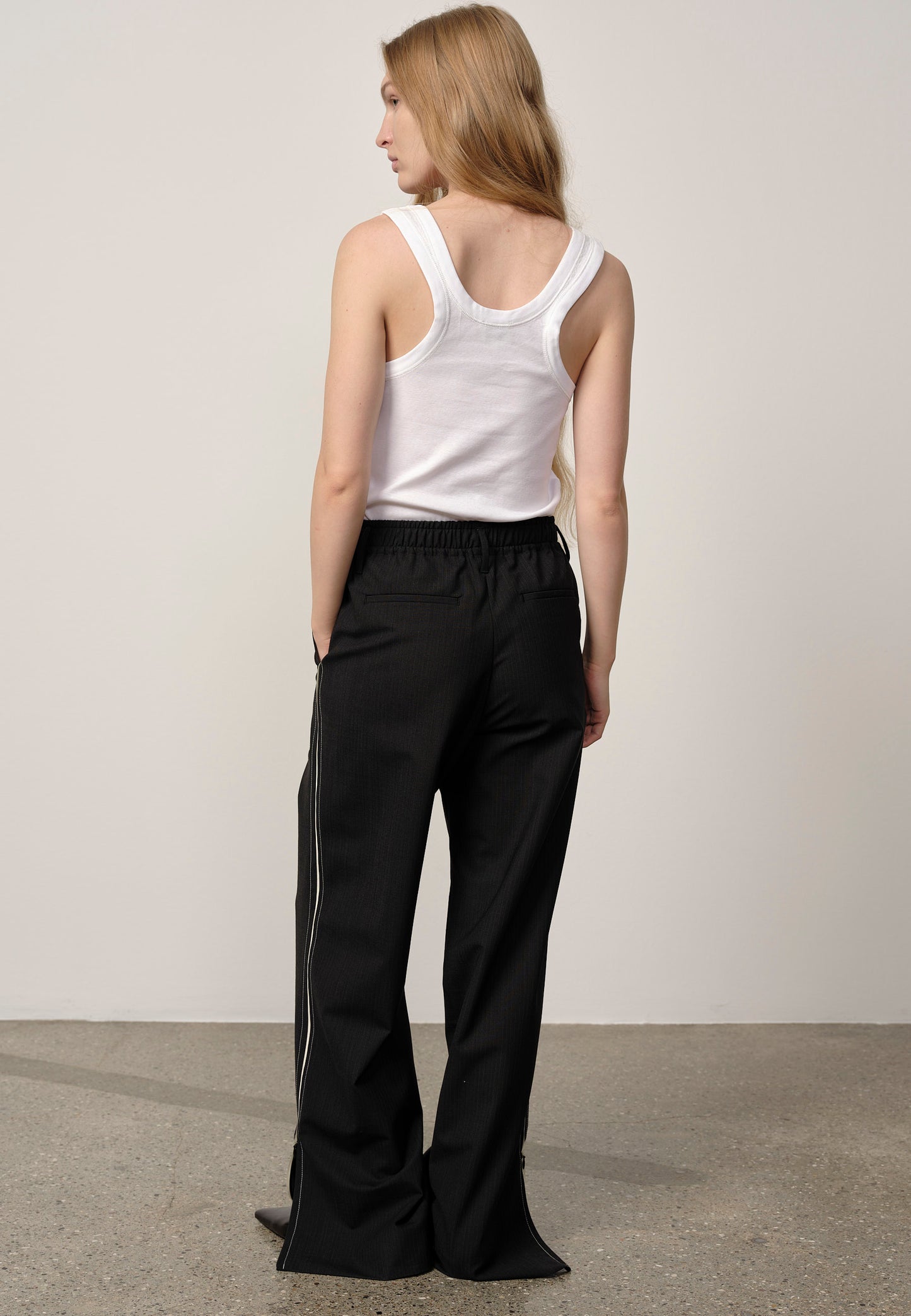 Person wearing a white tank top and black pants against a plain background