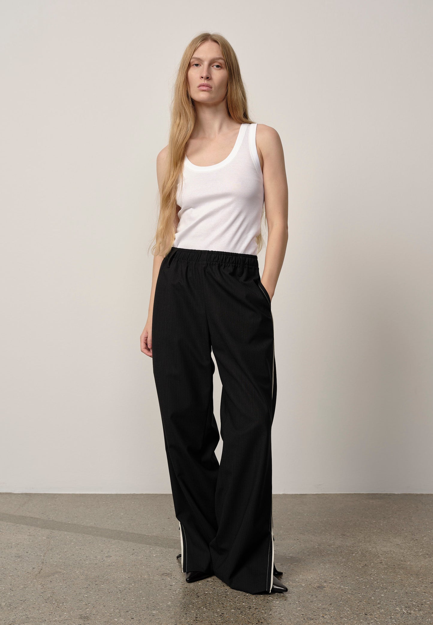 Woman wearing a white tank top and black wide-leg pants against a plain background