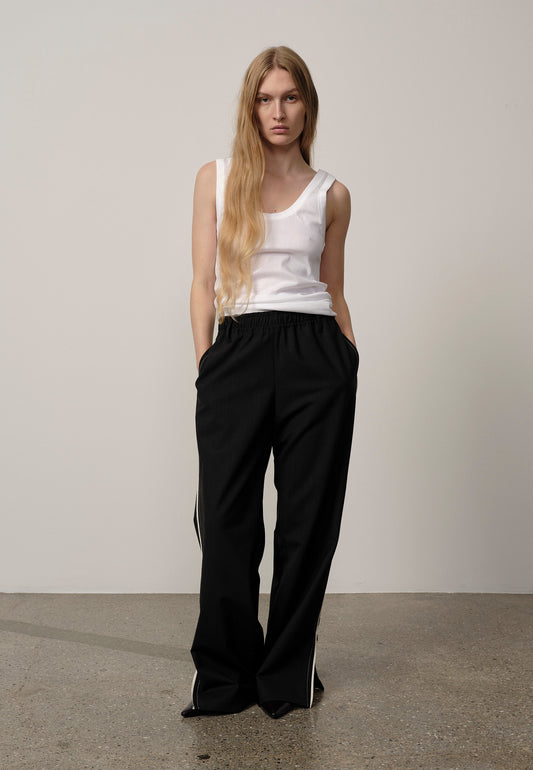 Woman wearing a white tank top and black pants against a plain background