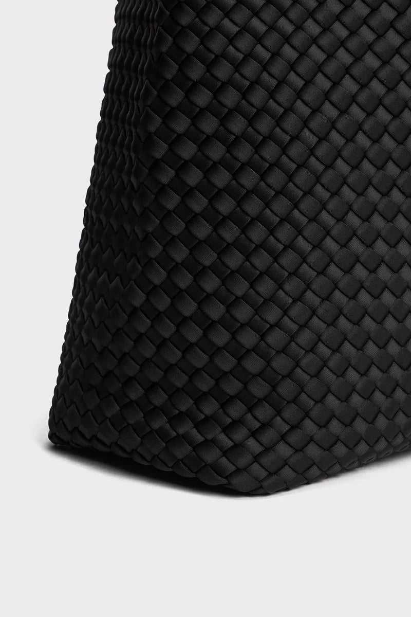 Close-up of a black woven leather bag corner showing the detailed basketweave texture against a light gray background.