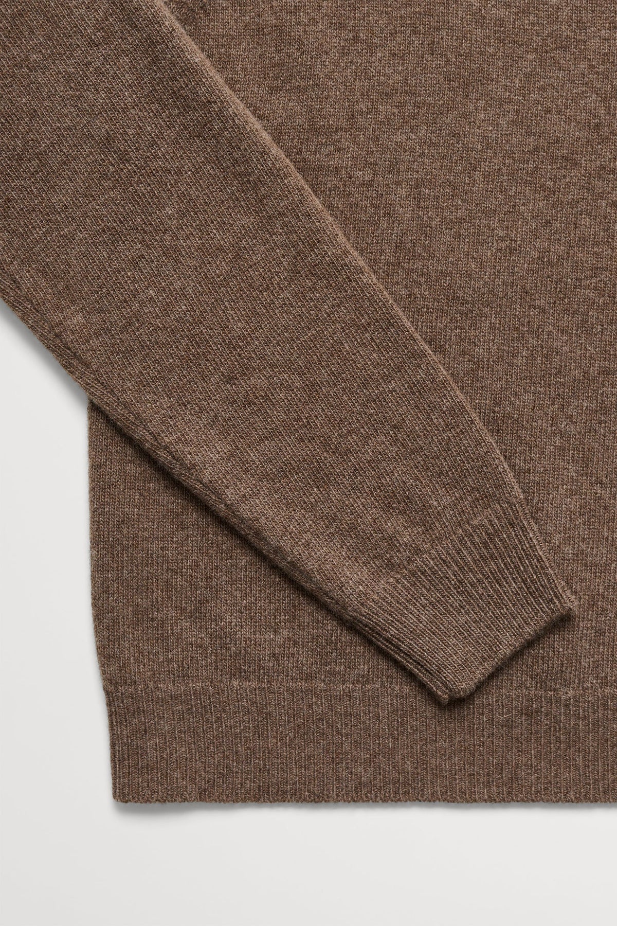 Close-up of a brown knit sweater showing the ribbed cuff and hem against a light gray background.