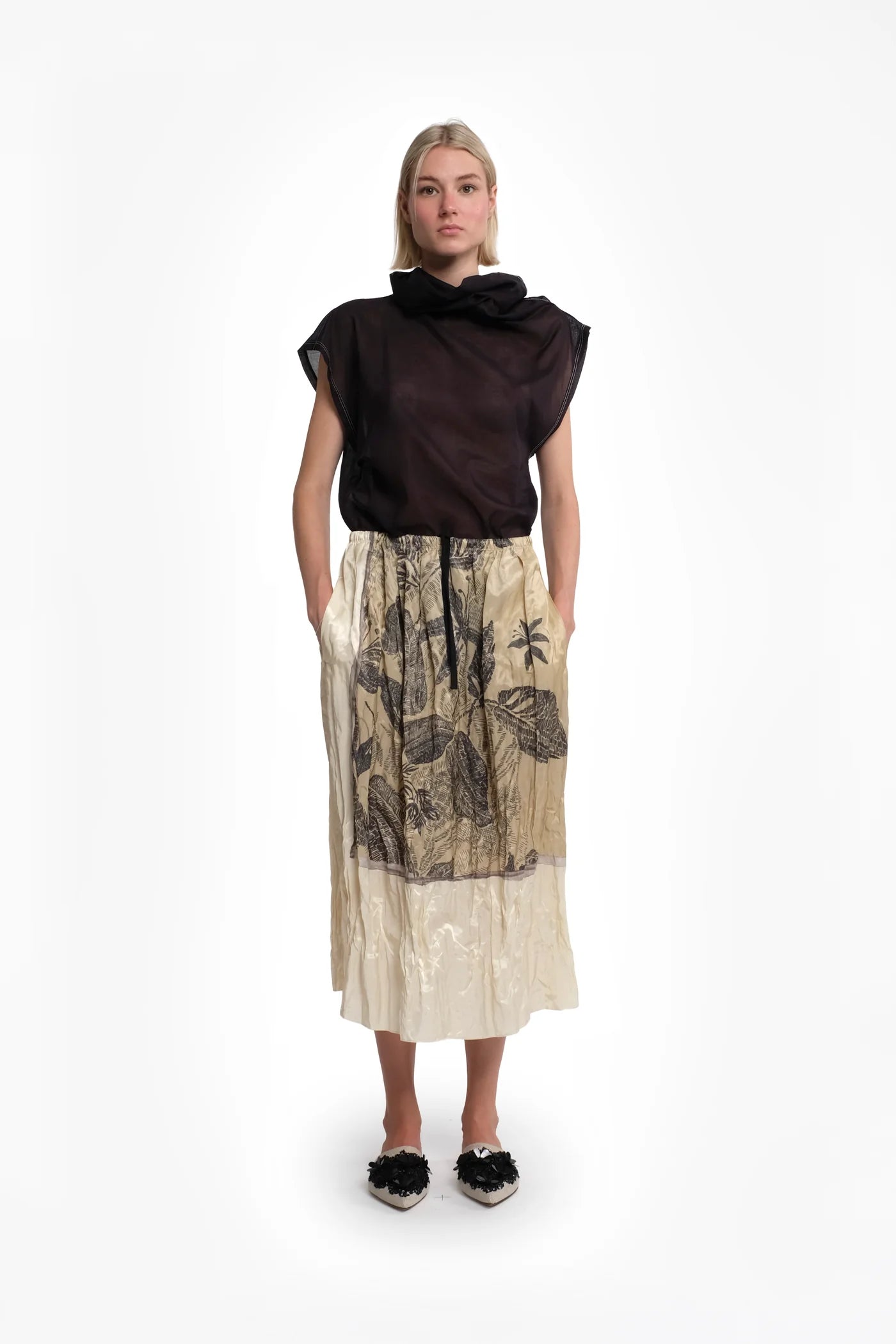 Woman wearing a black top and beige patterned skirt on a white background