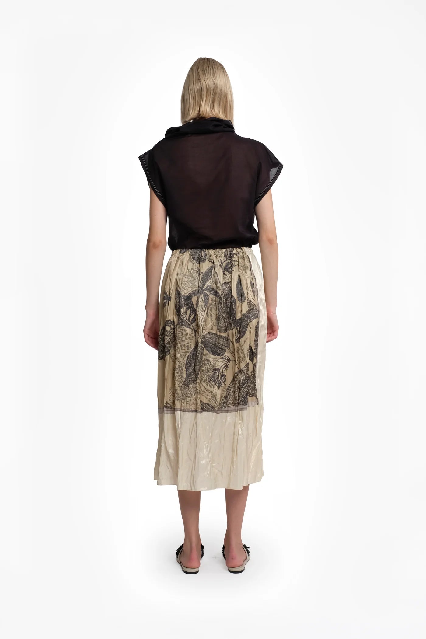 Person wearing a black top and patterned beige skirt on a white background