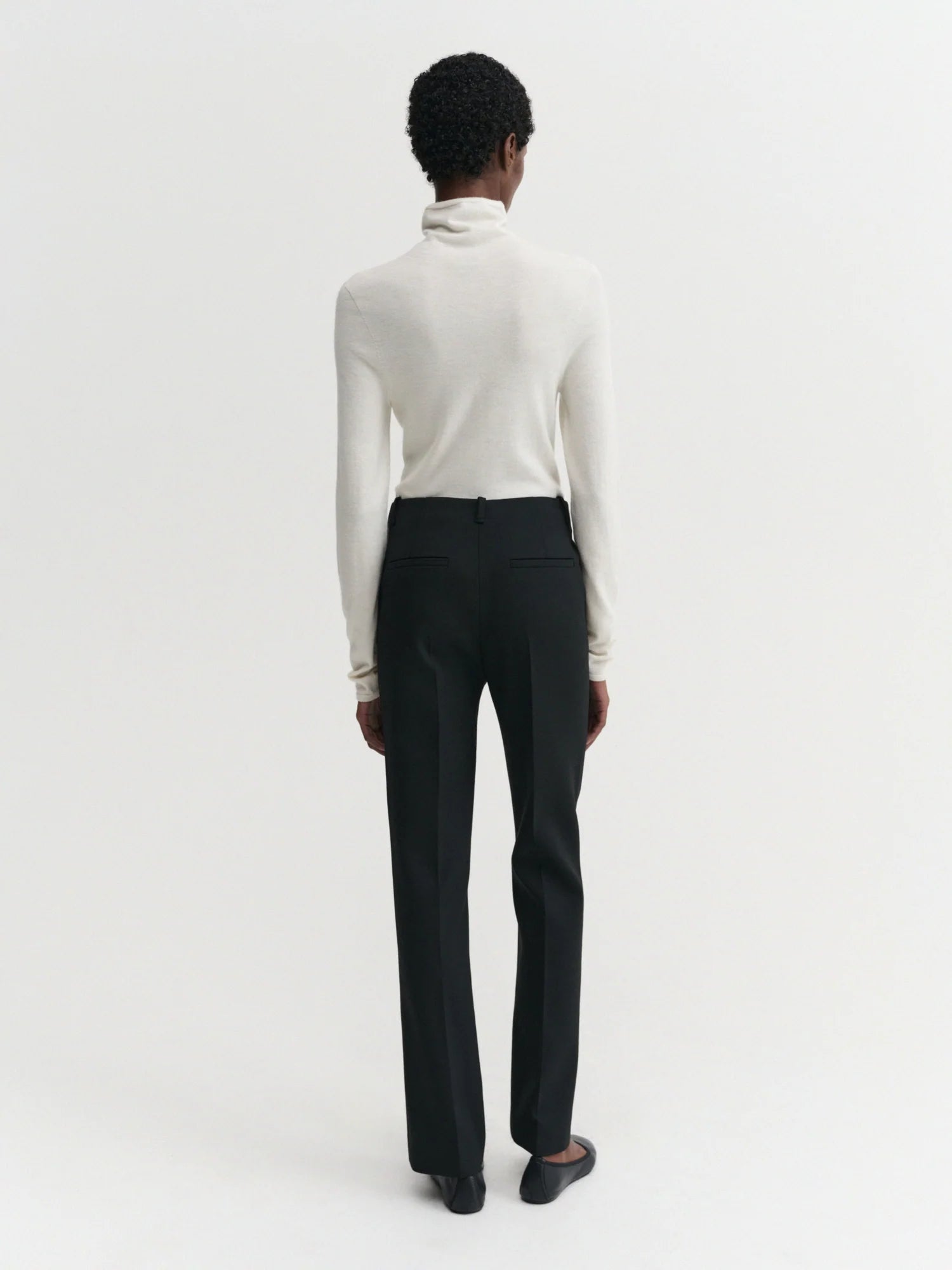 Person wearing a white turtleneck and black pants on a white background