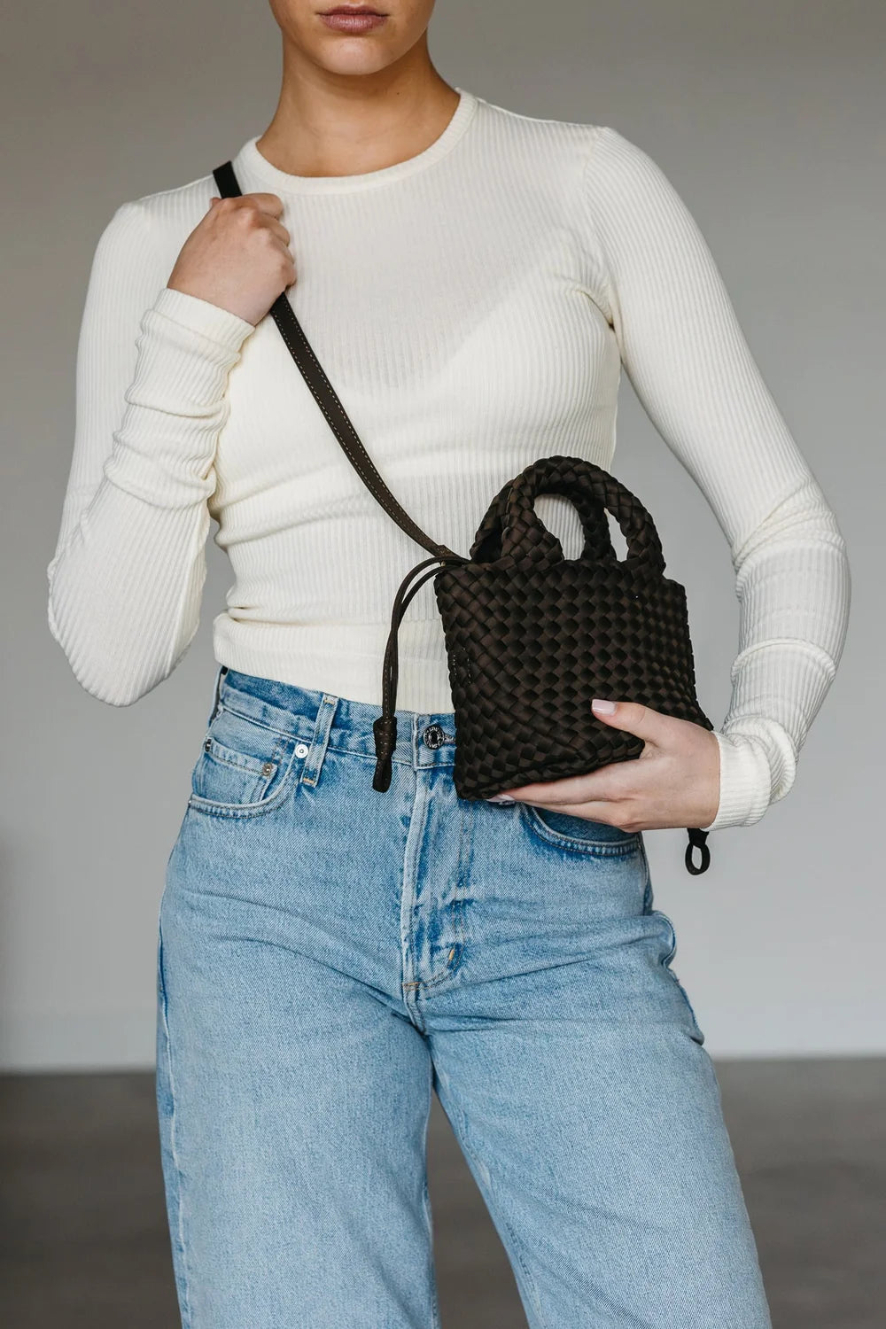 Person holding a black woven handbag against a neutral background
