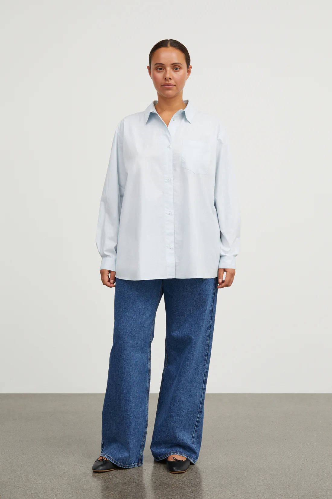 Person wearing a light blue shirt and blue jeans on a plain background