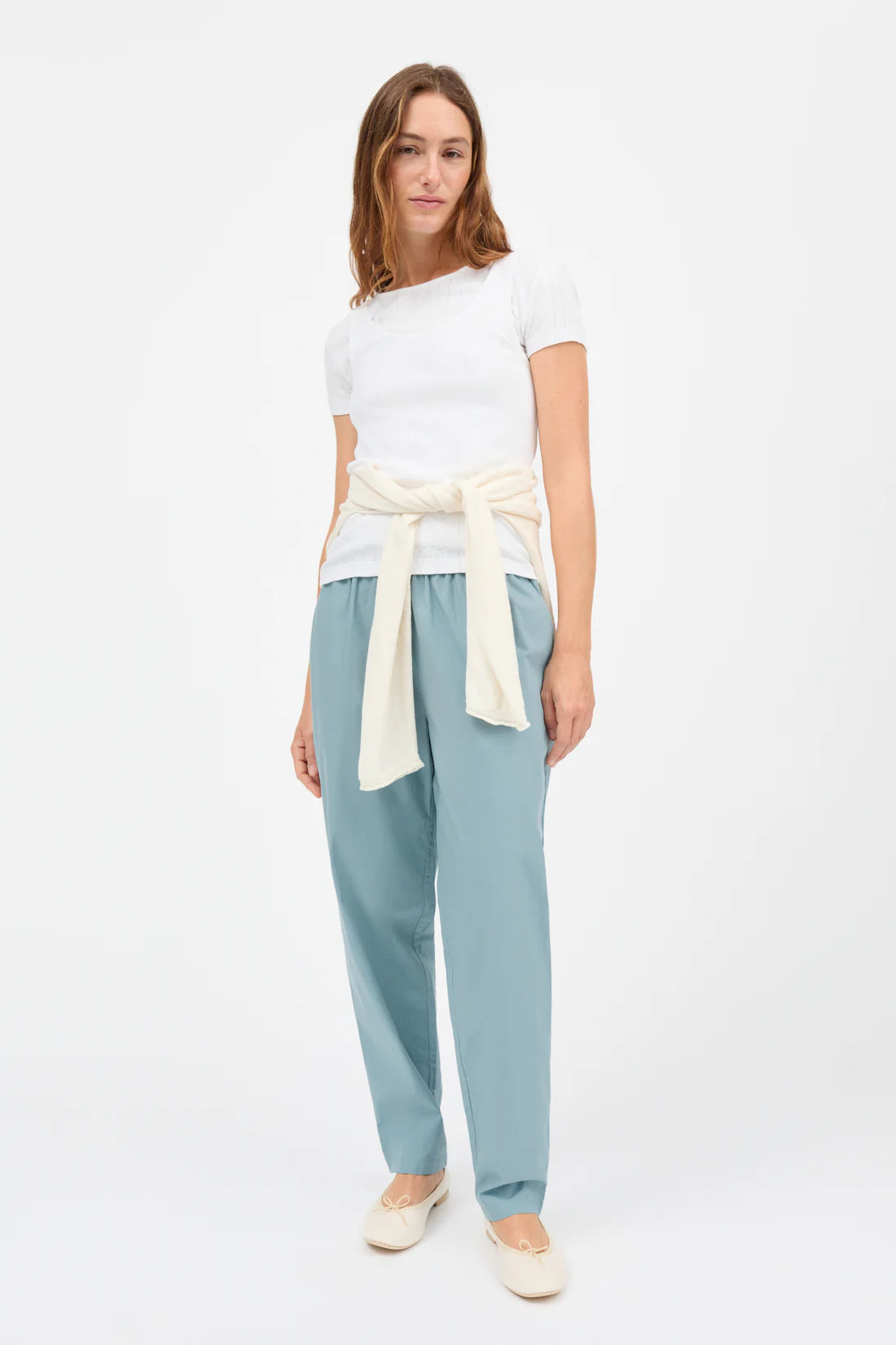 Woman wearing a white top and light blue pants with a cream belt on a white background