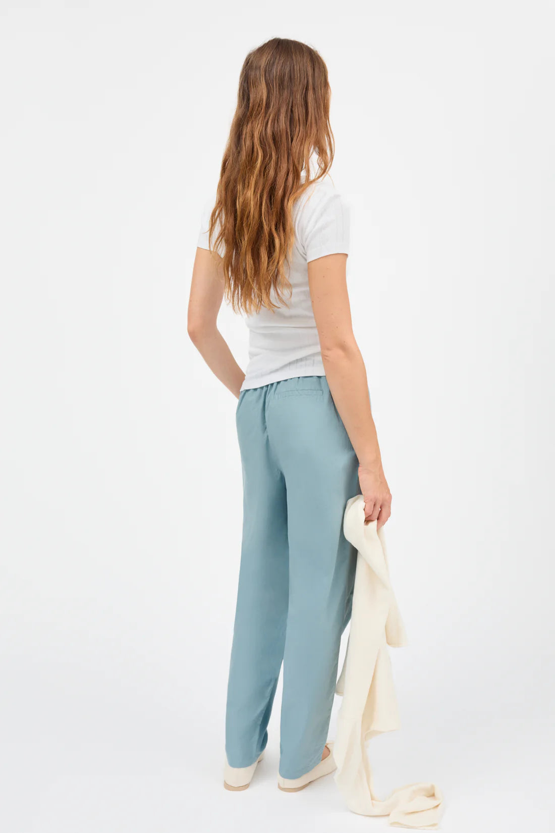 Woman wearing light blue pants and a white top on a white background