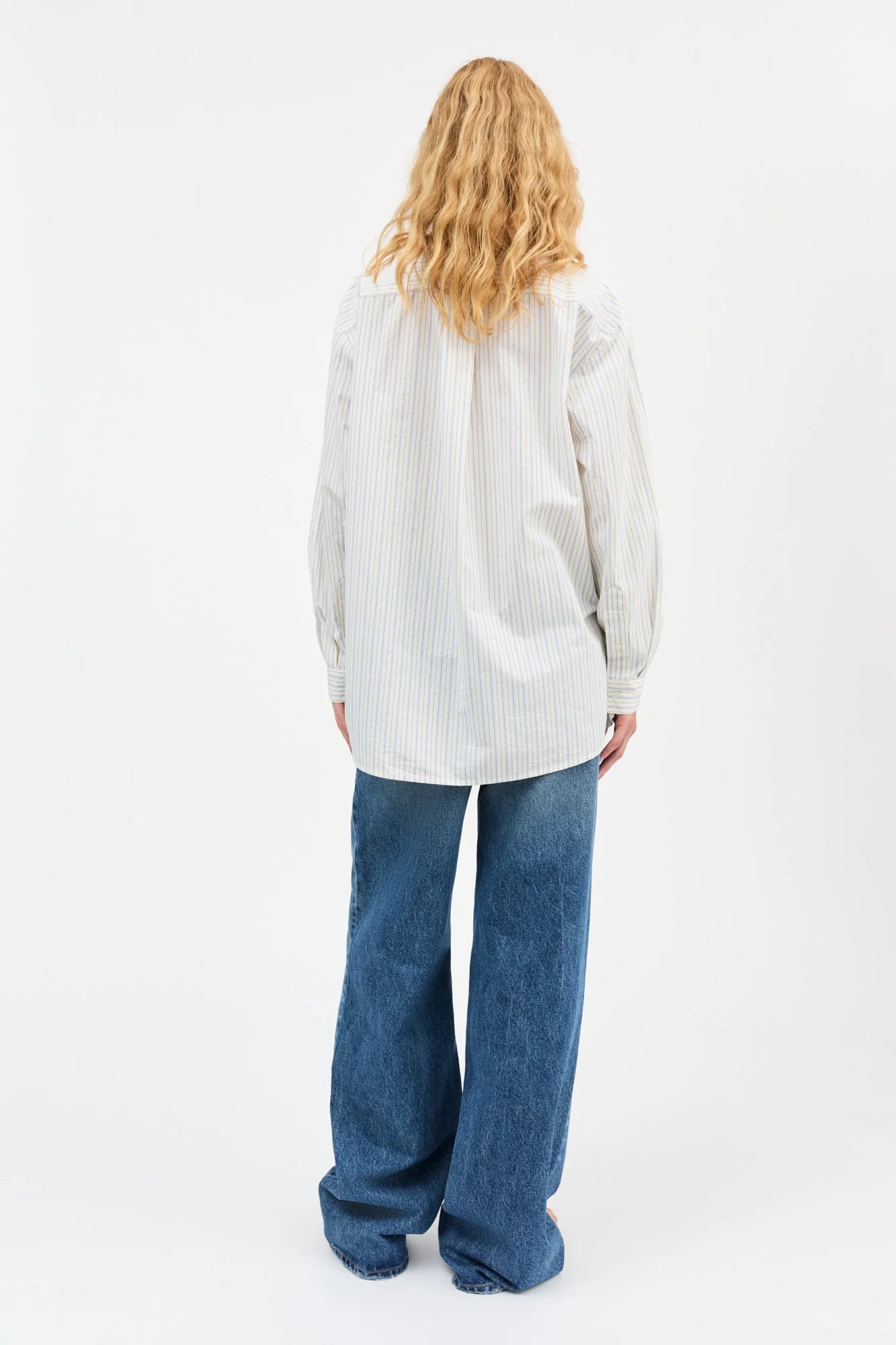 Person wearing a light-colored shirt and blue jeans on a white background