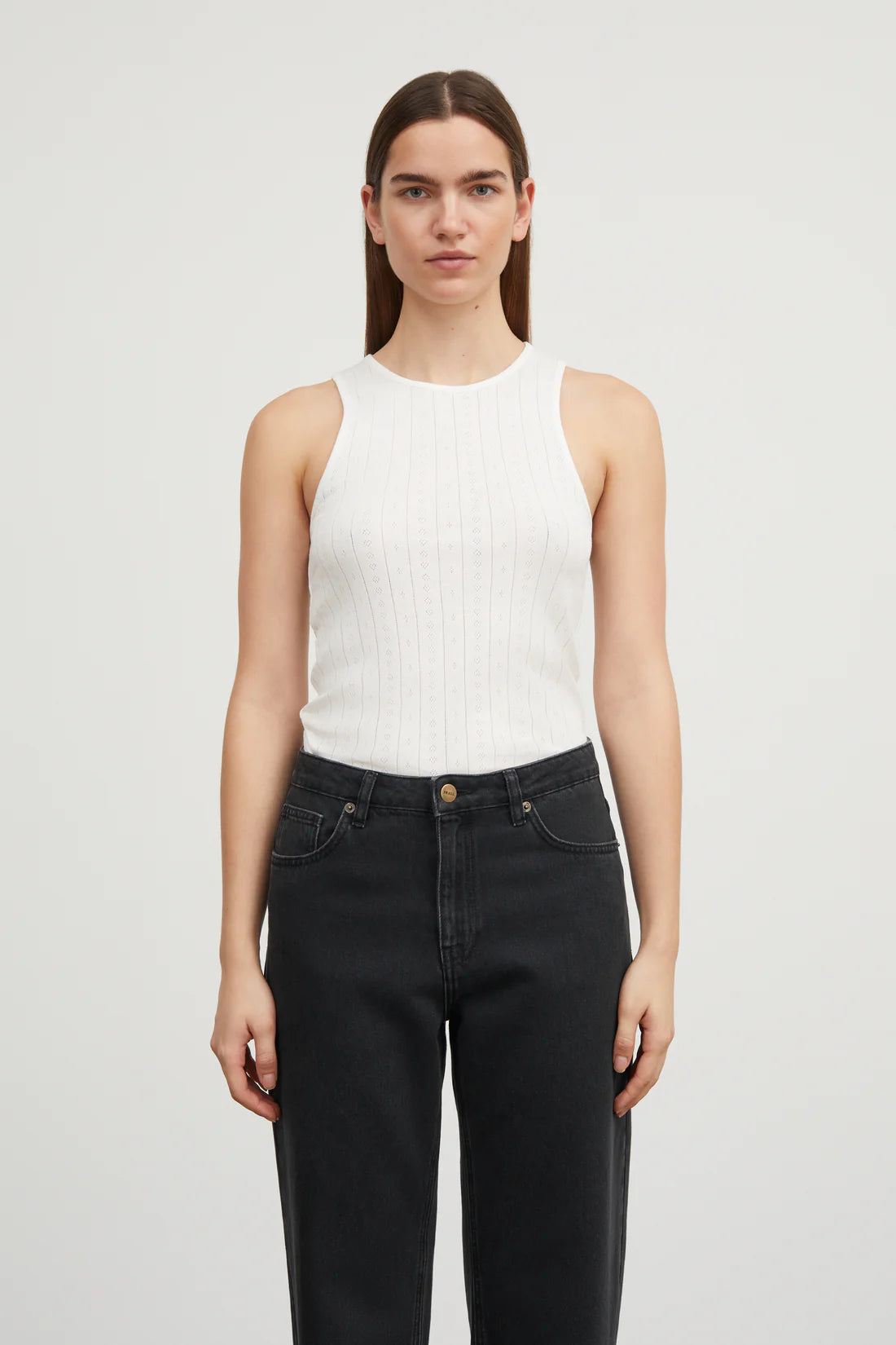 Woman wearing a white sleeveless top and black jeans on a light gray background