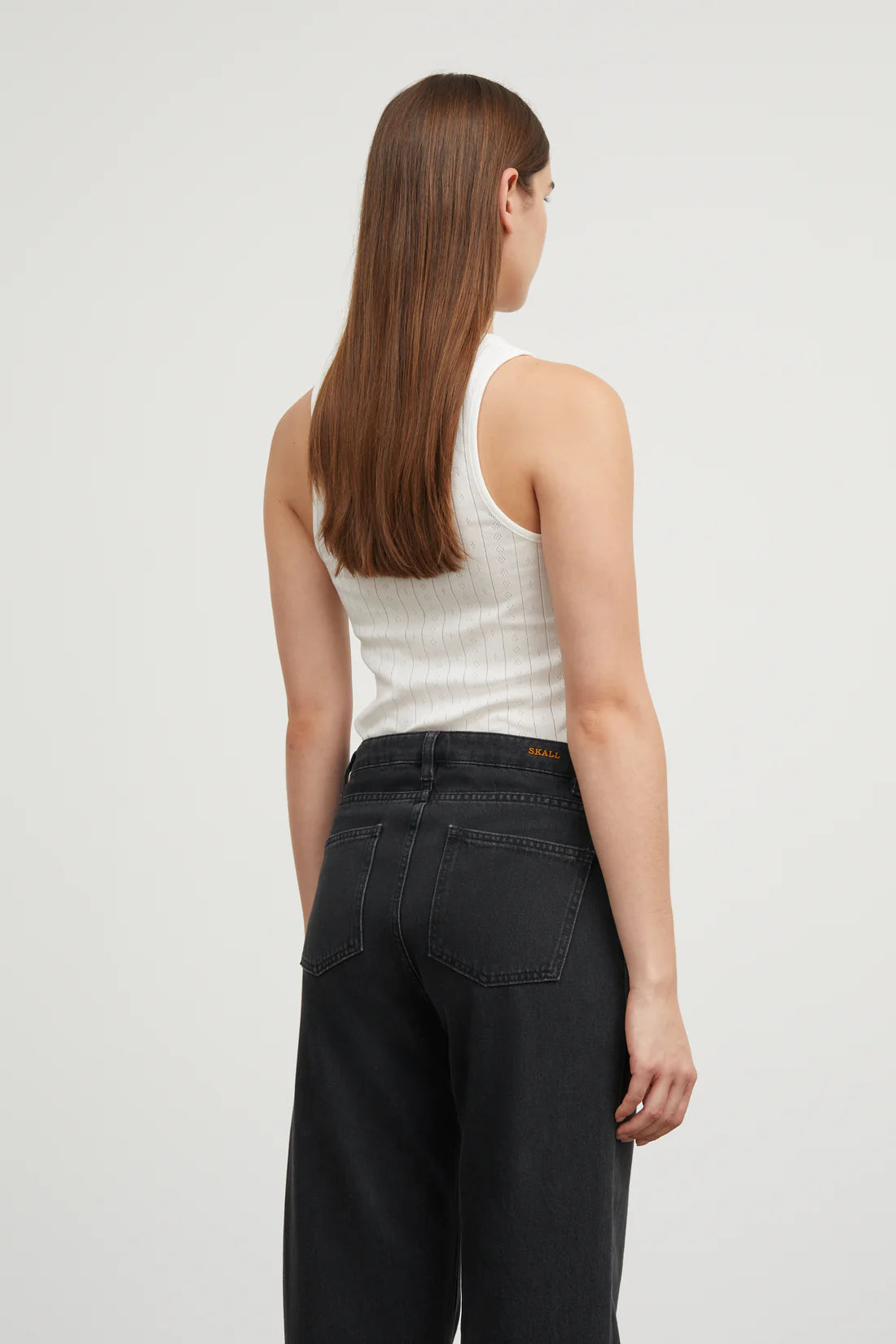 Woman wearing a white tank top and black pants on a light gray background