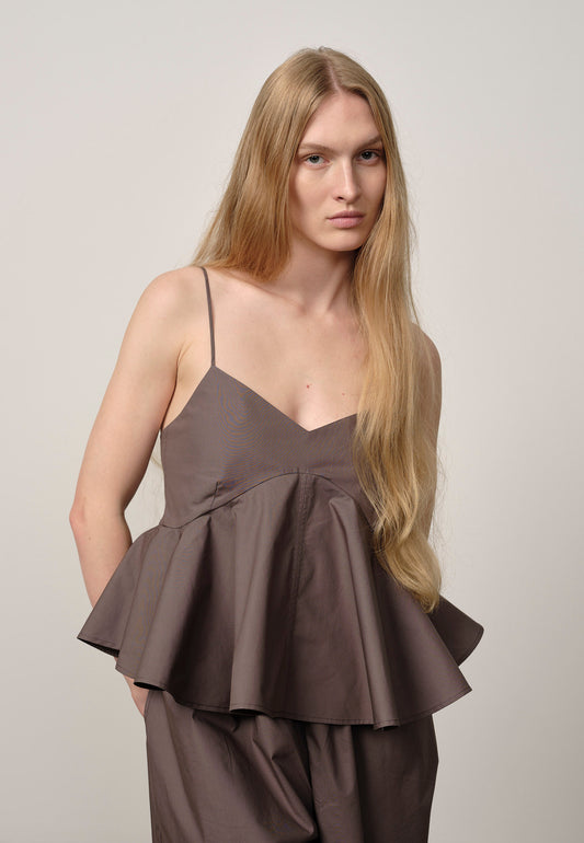 Woman wearing a brown peplum top and pants against a plain background