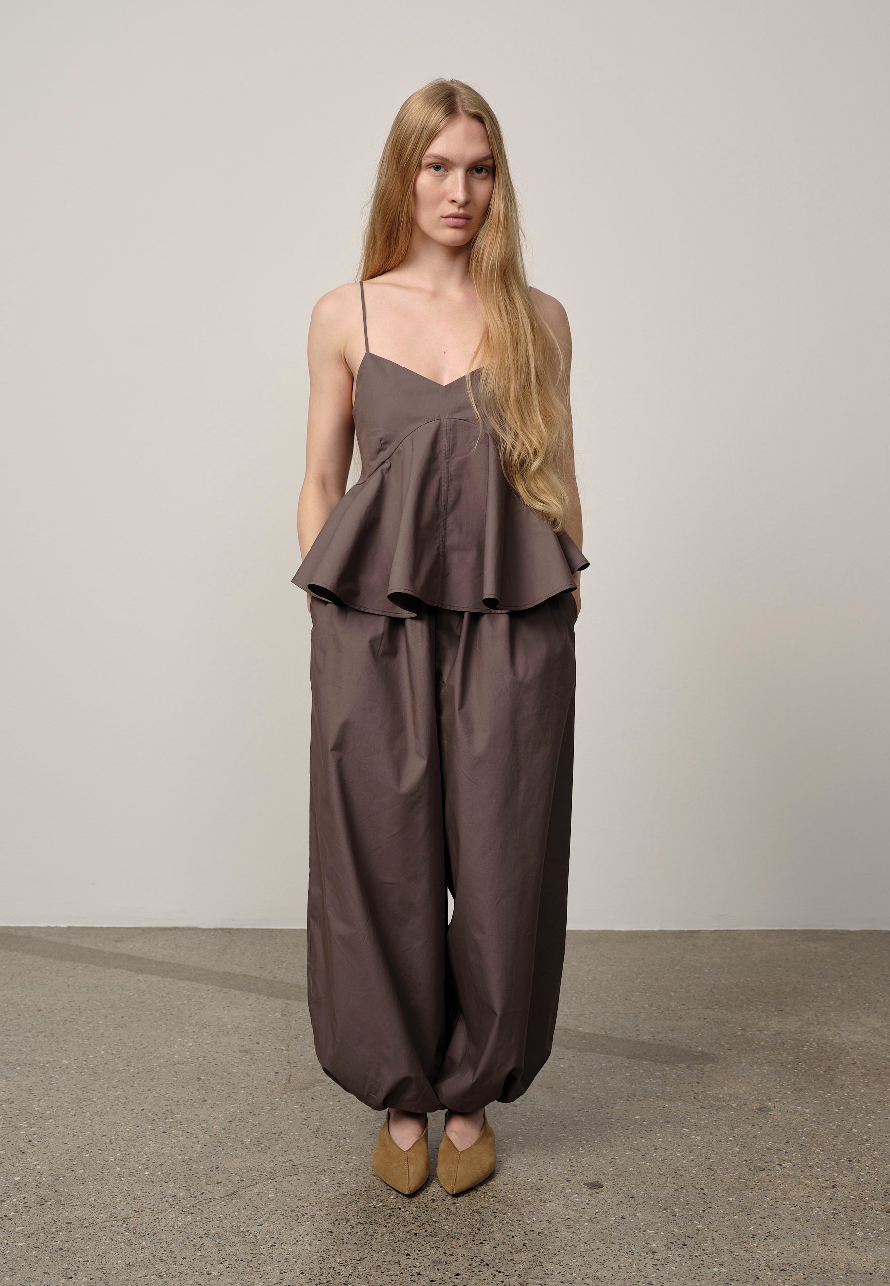 Woman wearing a brown peplum top and wide-leg pants against a plain background