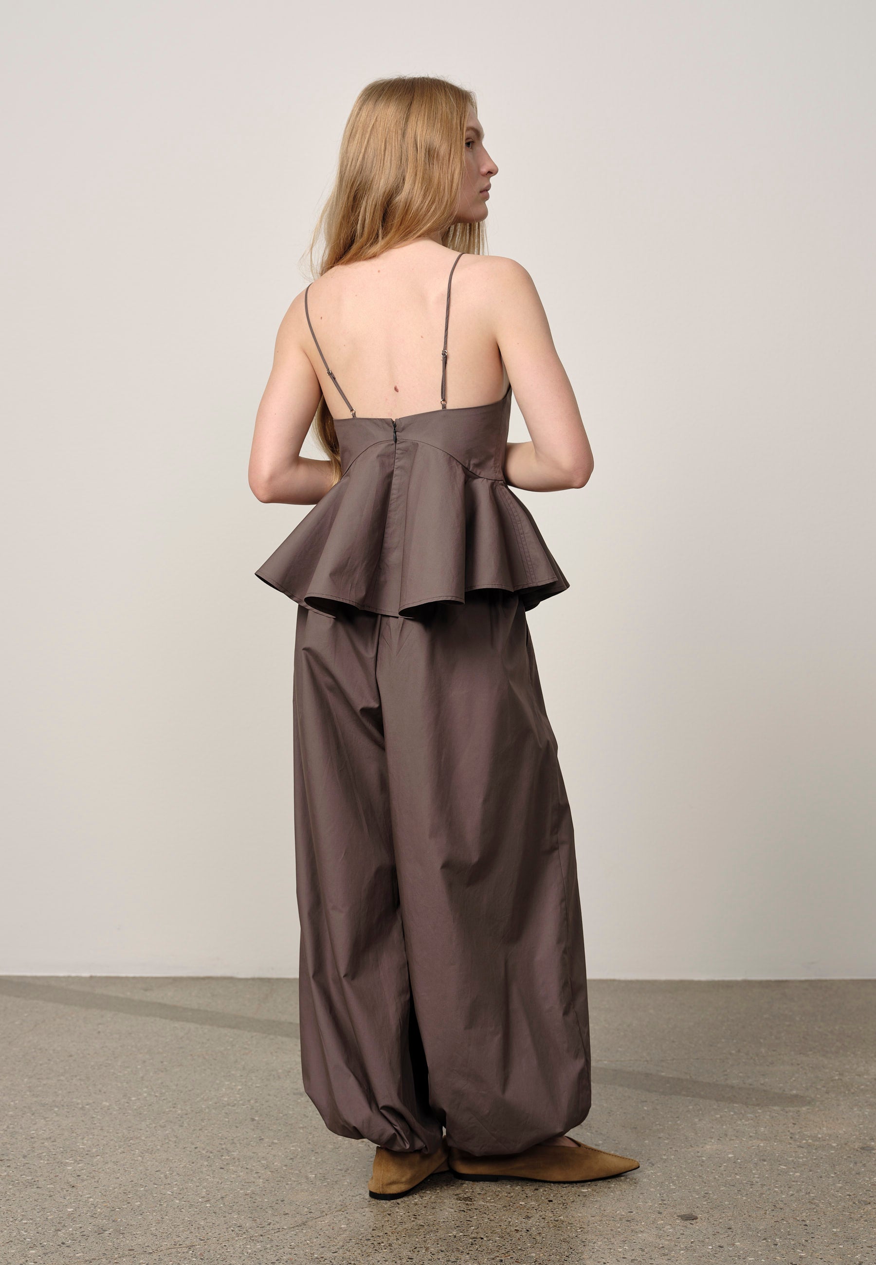 Woman wearing a brown peplum top and long skirt set against a plain background