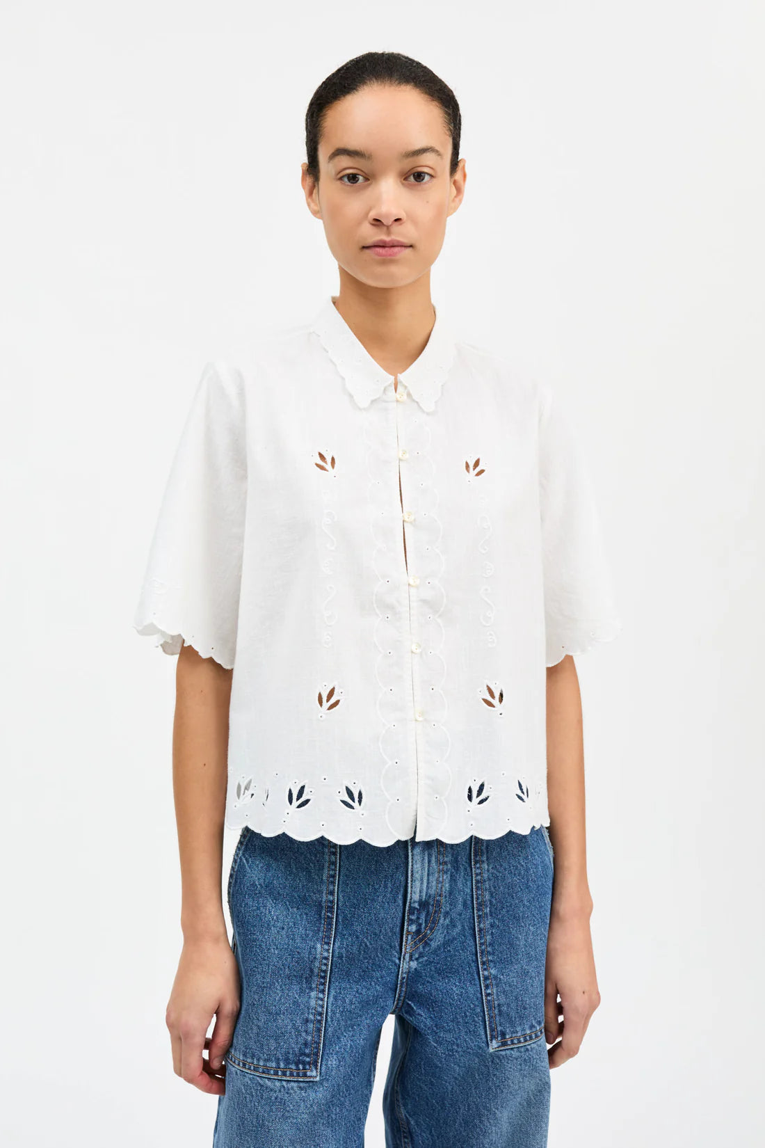 Person wearing a white blouse with floral embroidery and blue jeans on a white background