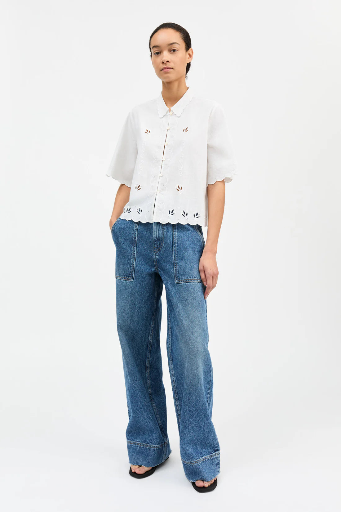 Person wearing a white blouse with floral details and blue jeans on a white background