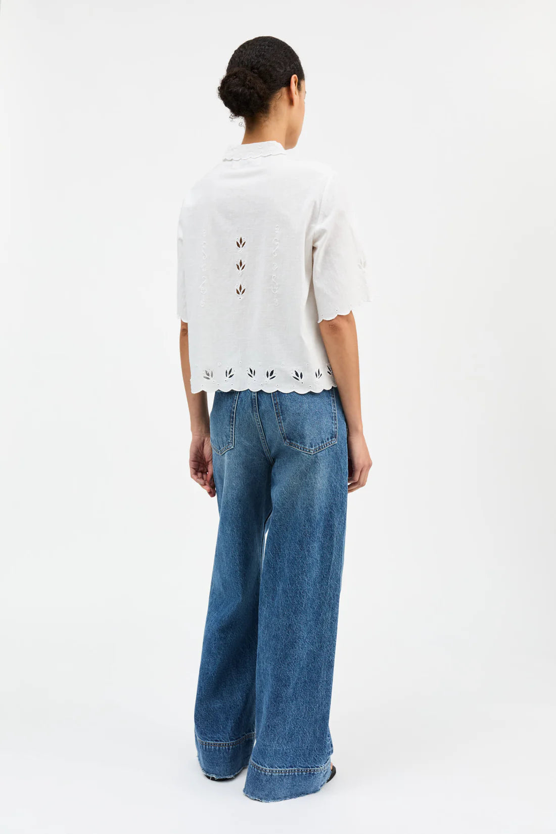 Person wearing a white blouse with black patterns and blue jeans on a white background