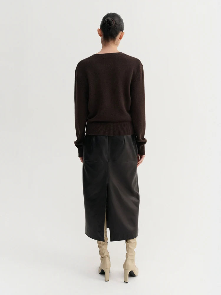 Person wearing a brown sweater and black leather skirt on a white background